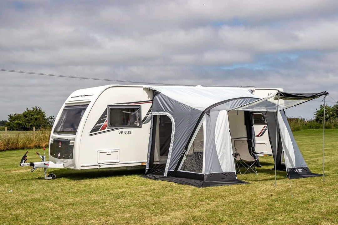 SunnCamp Swift Air 220 SC awning with an extended front sun canopy attached to a white Venus caravan, set on a grassy campsite beneath a cloudy sky.