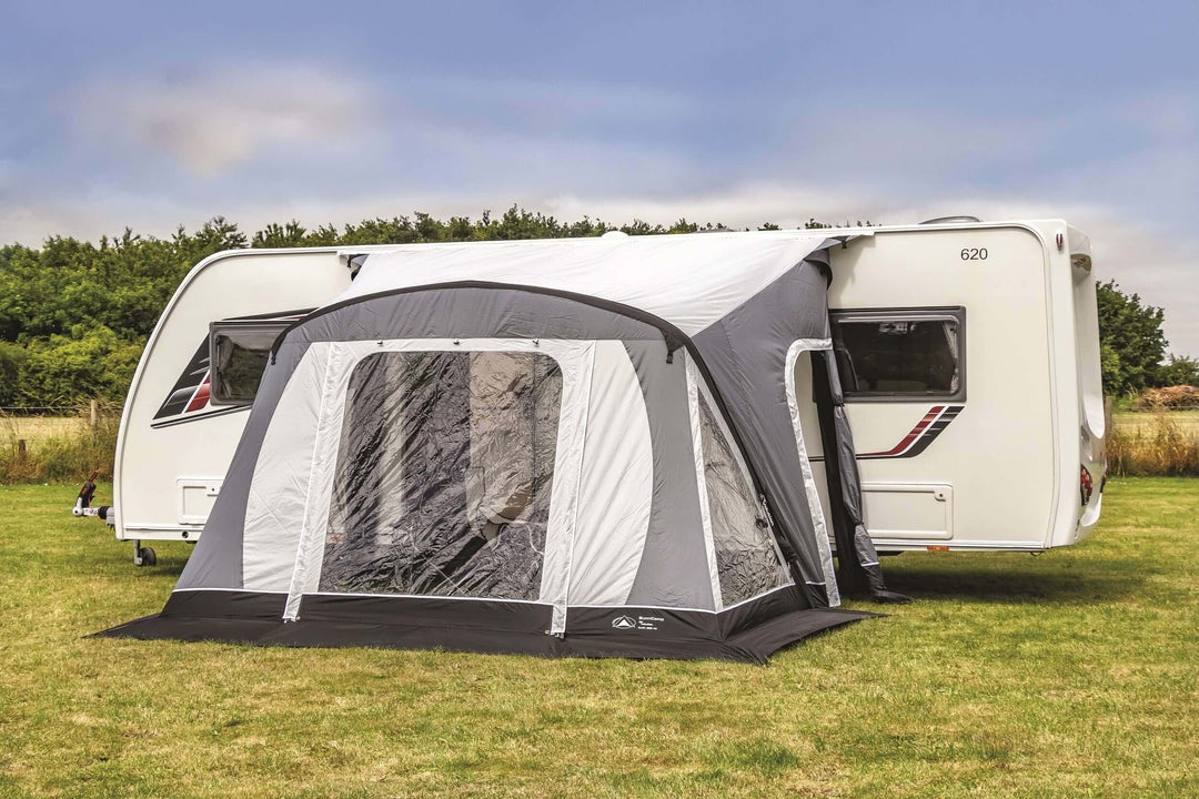 SunnCamp Swift Air 220 SC awning with a large covered entrance and clear window panels attached to a white Venus caravan, set on a grassy field beneath a partly cloudy sky.