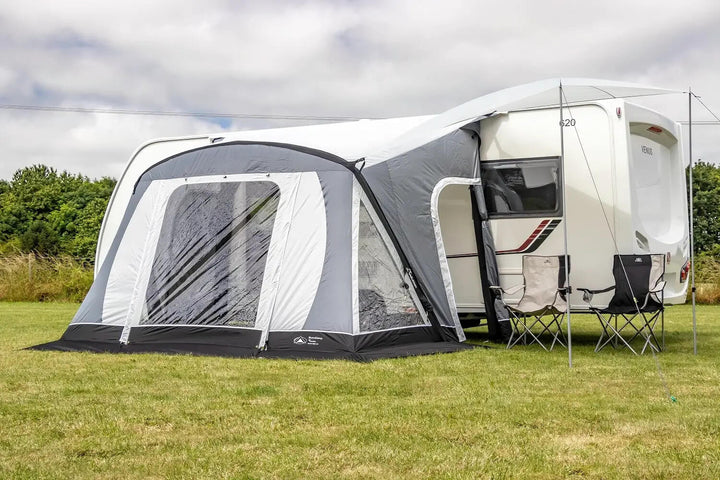 SunnCamp Swift Air 325 SC awning with a buckle-fit side sun canopy, offering extra shade beside a white Venus caravan with two folding camping chairs.