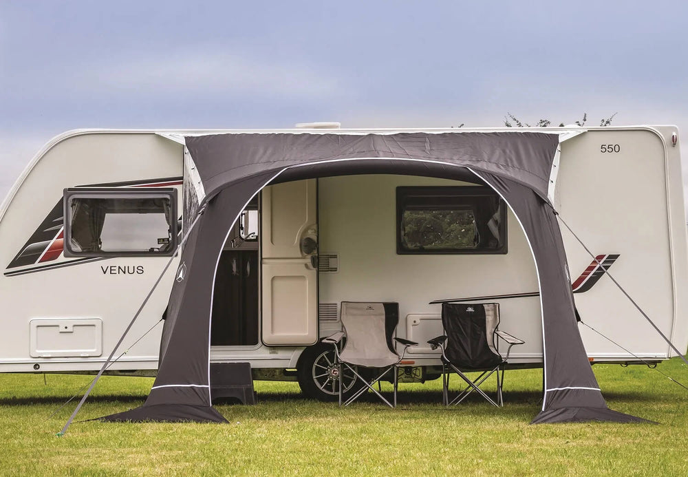 Front view of a SunnCamp Swift Air 325 canopy with a wide arched entrance, providing shaded outdoor seating beside a white Venus caravan on grass.