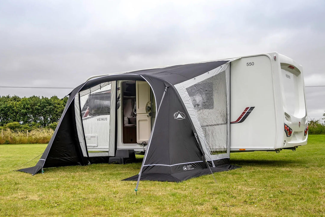SunnCamp Swift Air 390 caravan awning with a spacious arched entrance and clear window panels attached to a white Venus caravan, set on an open grassy field beneath a cloudy sky.