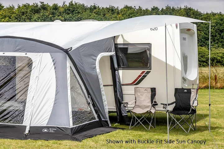 SunnCamp Swift Air 260 SC awning fitted with a buckle-fit side sun canopy, creating additional shade beside a white Venus caravan with two folding camping chairs underneath.