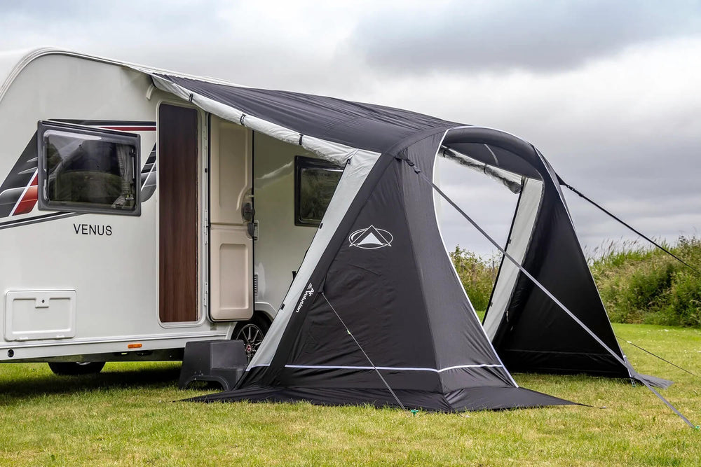 Close-up view of the black and grey SunnCamp Swift Air 260 awning with an open arched entrance and clear window panels, attached to a white caravan on grass.