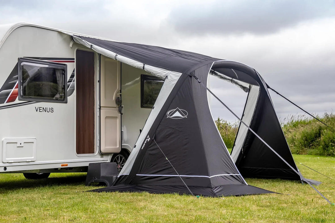 Close-up view of the black and grey SunnCamp Swift Air 260 awning with an open arched entrance and clear window panels, attached to a white caravan on grass.