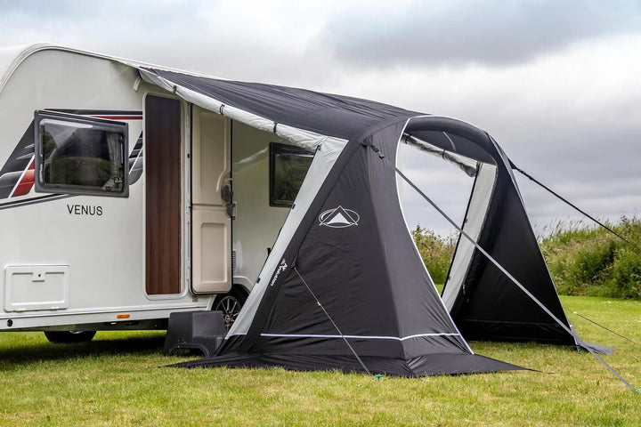 Close-up view of the black and grey SunnCamp Swift Air 260 awning with an open arched entrance and clear window panels, attached to a white caravan on grass.