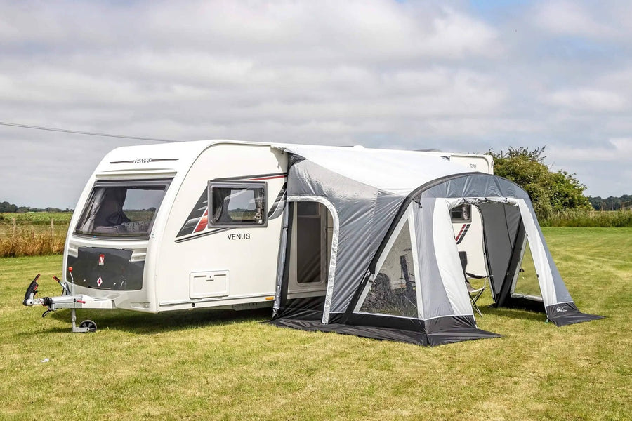 SunnCamp Swift Air 325 SC awning attached to a white Venus caravan, featuring grey and white panels, clear windows and an open front entrance on a grassy campsite.