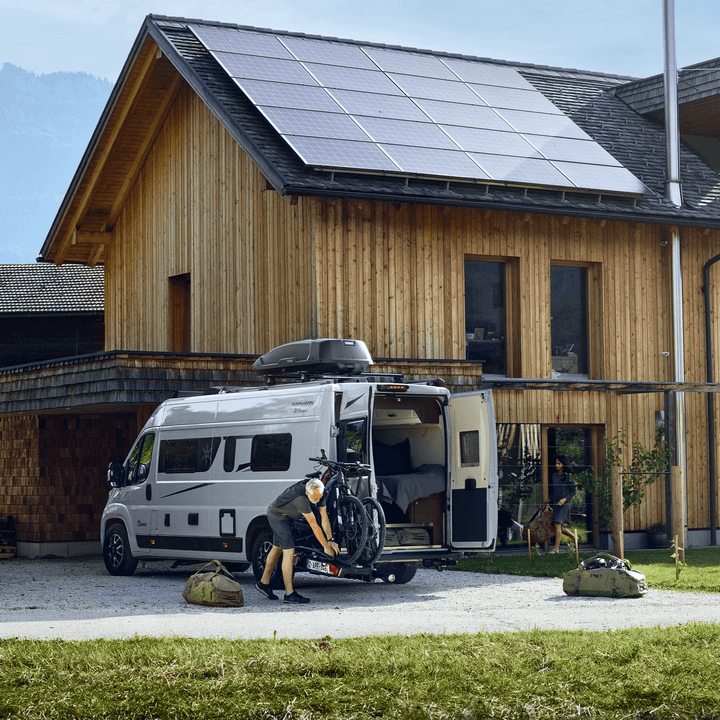 Man loading bicycles on Thule Veloswing towbar outside a wooden house on an outdoor background.