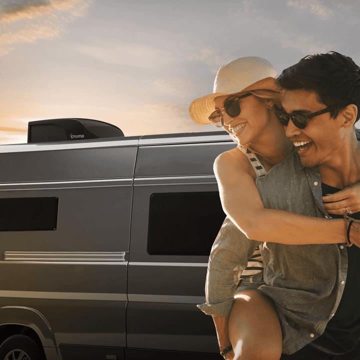 Couple enjoying sunset beside a camper van equipped with a Truma Aventa Compact Plus rooftop air conditioner in black finish.