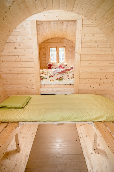 Interior view of a Viking Industrier 2.2 x 4m Sleeping Barrel showing a single bed in the foreground and a floral double bed setup in the background, natural wood finish.