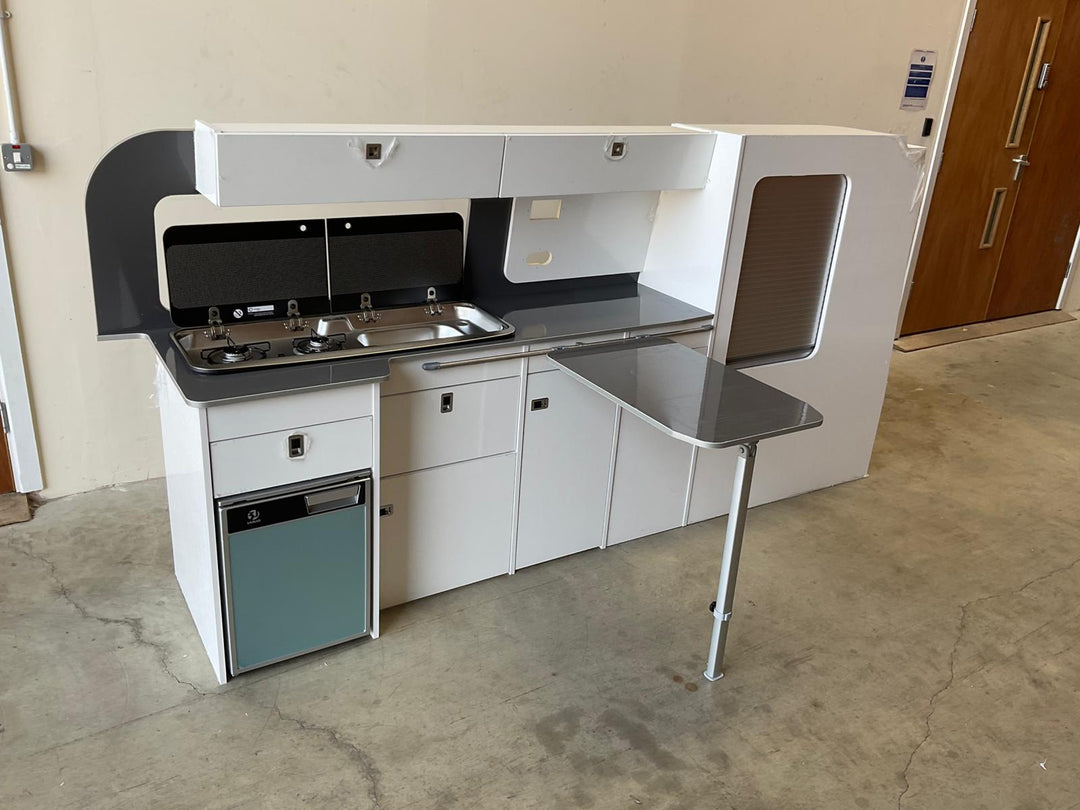 VW Transporter T5/T6 Campervan Kitchen Unit Bespoke in light grey finish with pull-out table, displayed on a concrete floor against a white wall.