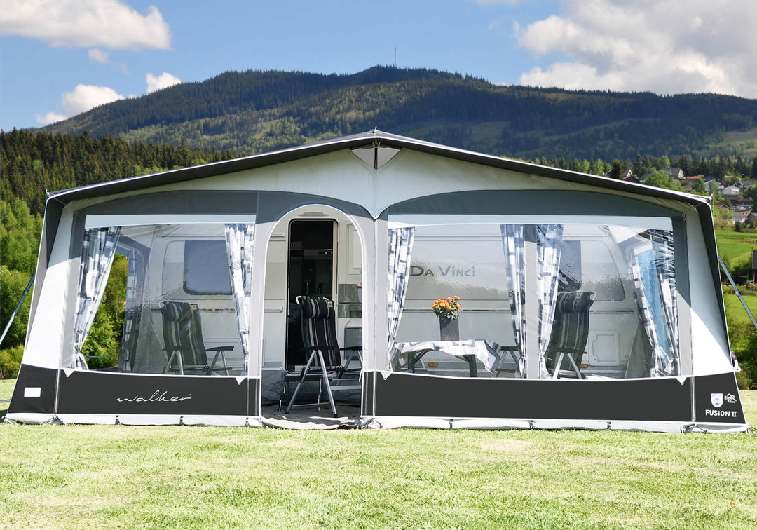 Front view of Walker Fusion 2 Caravan Awning with large panoramic windows and striped curtains on a campsite with hills in the background.